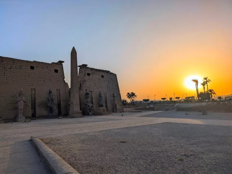 Entrée du temple de Louxor avec son obélisque et ses colosses, sous un ciel orangé